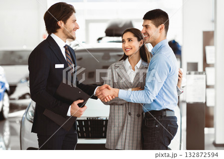 Fair Deal. Happy Man Shaking Hands With Car Sales Manager Buying Auto With Wife In Automobile Dealership Store Fair Deal. Happy Man Shaking Hands With Car Sales Manager Buying Auto With Wife In Automobile Dealership Store 132872594