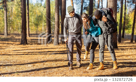 Multiracial guys supporting their female friend with injured anckle, hiking together at forest, free space 132872726