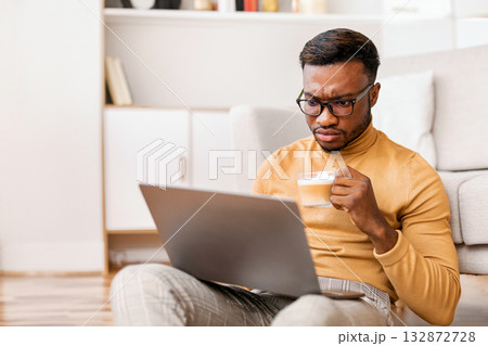 Serious Afro Businessman Using Laptop Reading Business News Having Morning Coffee Working From Home Sitting On Floor Indoor 132872728