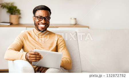 Weekend. African American Man In Eyeglasses Holding Digital Tablet And Smiling To Camera Sitting On Couch At Home. Selective Focus 132872782
