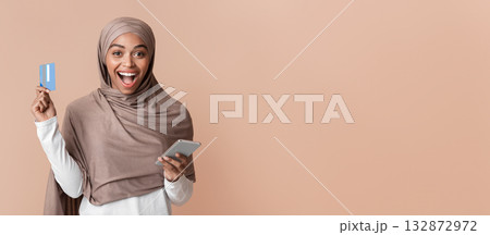 Online Shopping App. Overjoyed Black Muslim Girl In Hijab Holding Credit Card And Smartphone, Enjoying Internet Sales, Yellow Background, Free Space Online Shopping App. Overjoyed Black Muslim Girl In Hijab Holding Credit Card And Smartphone, Enjoying Internet Sales, Yellow Background, Free Space 132872972