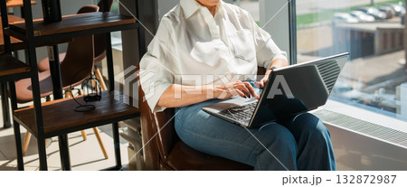 Woman typing on laptop near window in bright cafe interior. Banner with copy space and empty place for advertising. Focus, creativity, and productive work atmosphere in modern lifestyle. 132872987