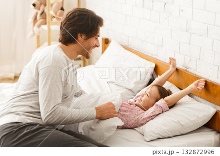 Preschool girl stretching in bed after waking up, smiling to her young dad, home interior 132872996
