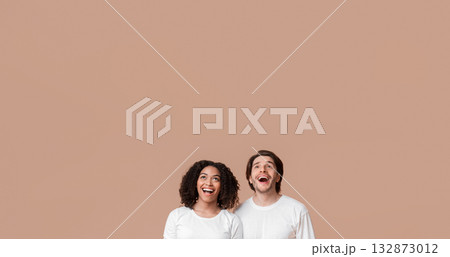 Excited interracial couple looking upwards in amazement, standing over yellow background with free space Excited interracial couple looking upwards in amazement, standing over yellow background with free space 132873012