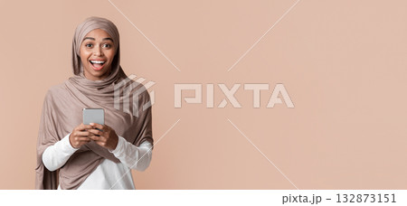 Good message. Excited black islamic girl in headscarf holding smartphone in hands and looking at camera, received nice news, yellow background 132873151