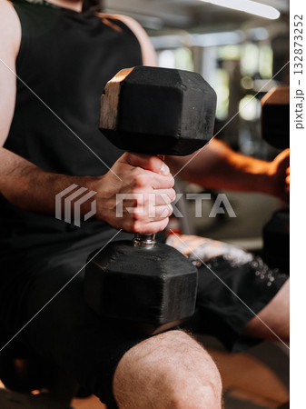 Close-up of male hand holding heavy dumbbell during strength workout in gym Close-up of male hand holding heavy dumbbell during strength workout in gym 132873252