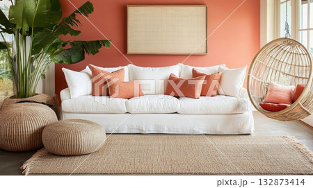 A stylish living area features a comfortable white sofa adorned with orange cushions, surrounded by natural textures. A hanging chair and large plants create a warm, inviting atmosphere. A stylish living area features a comfortable white sofa adorned with orange cushions, surrounded by natural textures. A hanging chair and large plants create a warm, inviting atmosphere. 132873414