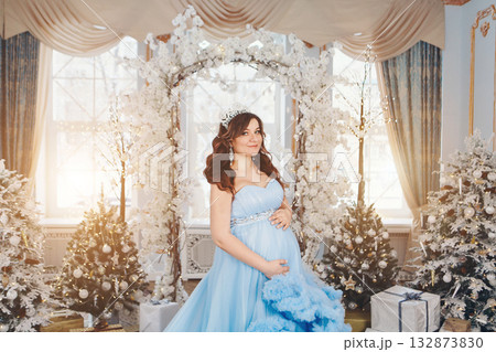 pregnant girl in a lush blue dress. girl with dark hair wearing a crown. christmas decoration. High quality photo 132873830