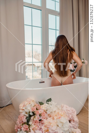 Woman bathtub bathroom, female standing in modern white freestanding bathtub looking out large window, peaceful self-care moment. Woman bathtub bathroom, female standing in modern white freestanding bathtub looking out large window, peaceful self-care moment. 132876217