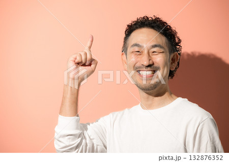 オレンジ背景で指を差すポイントポーズをする爽やかな髭のミドル男性 132876352