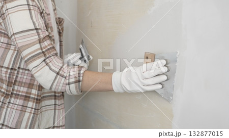 Unknown female construction worker wearing protective gloves applying plaster, smoothing wall surface during home renovation work Unknown female construction worker wearing protective gloves applying plaster, smoothing wall surface during home renovation work 132877015