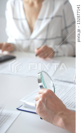 Groupe of professional accountants working together, using a magnifying glass and a calculators, to audit financial reports in their brightly lit office. Audit and taxes concept 132877141
