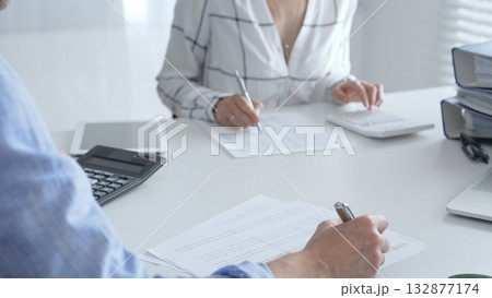 Accounting team working together, reviewing financial reports, using calculator, analyzing data while working at sleek corporate workspace. Audit and taxes concept 132877174