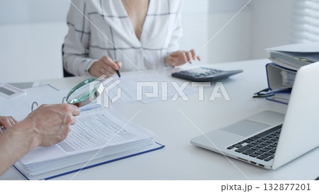 Two professional accountants working together, using a magnifying glass and a calculators, to audit financial reports in their brightly lit office. Audit and taxes in business 132877201
