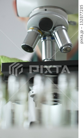 Close up of a scientist in green gloves and a mask using a microscope for research and analysis in a laboratory setting. Medicine, healthcare and science concept 132877285
