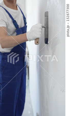 Professional construction worker wearing blue work overall is using a finishing trowel to carefully apply plaster on a wall, demonstrating expertise in home renovation and interior finishing 132877300