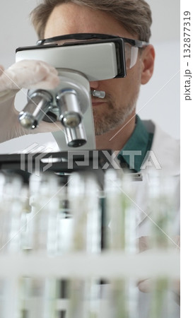 Man scientific researcher in protective gear analyzing specimens through a microscope in a sterile laboratory environment. Medicine, health care and science concept 132877319