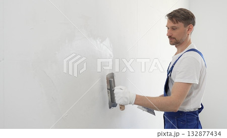 Professional male construction worker is using a finishing trowel to carefully apply plaster on a wall, demonstrating expertise in home renovation and interior finishing. Portrait view Professional male construction worker is using a finishing trowel to carefully apply plaster on a wall, demonstrating expertise in home renovation and interior finishing. Portrait view 132877434