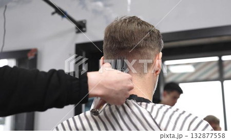 Professional hairstylist trimming client's hair using electric clippers, creating sleek, contemporary haircut with expert technique in modern barbershop setting Professional hairstylist trimming client's hair using electric clippers, creating sleek, contemporary haircut with expert technique in modern barbershop setting 132877558
