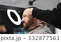 Skilled barber carefully grooming client's beard with electric razor, creating precise, trendy look inside contemporary barbershop setting 132877561