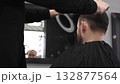 Professional barber trimming dark heard male client's hair with scissors and comb, creating precise modern hairstyle inside contemporary grooming salon 132877564