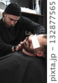 Professional barber carefully shaving client's beard with straight razor, applying gel and using hot towel in barbershop setting, vertical view 132877565