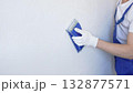 Unknown male construction worker wearing protective white gloves and blue construction coveralls, is sanding white wall with blue hand block, preparing smooth surface during interior home renovation 132877571