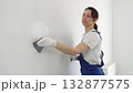 Construction worker woman spreading finishing putty on white wall, wearing protective gloves while smoothing surface with putty knife for precise home repair 132877575
