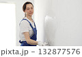 Professional female construction worker wearing blue coveralls is using a finishing trowel to carefully apply plaster on a wall, demonstrating expertise in home renovation 132877576