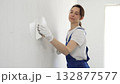 Construction worker woman spreading finishing putty on white wall, wearing protective gloves while smoothing surface with putty knife for precise home repair 132877577