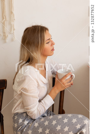 Woman holding mug and looking aside while sitting at home in peaceful atmosphere. Reflection, rest and mindfulness in modern life. 132877652