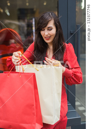 Happy woman searching through shopping bags outdoor. Consumer joy, lifestyle and leisure shopping culture. Happy woman searching through shopping bags outdoor. Consumer joy, lifestyle and leisure shopping culture. 132877746