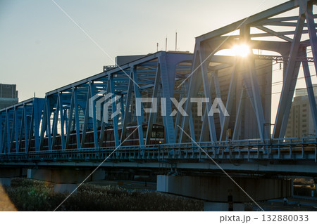 真っ青な冬の青空の中の沈みゆく夕日が差し込む鉄橋　東京の多摩川の六郷土手にて 132880033