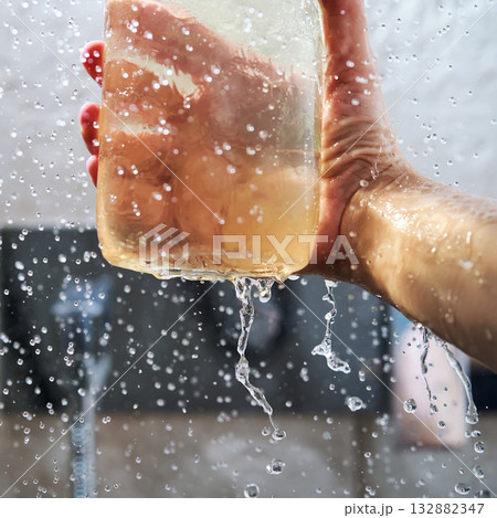 Hand holding jar with shower gel splashing and drops Hand holding jar with shower gel splashing and drops 132882347