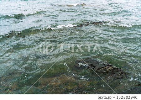 Clear lake waves rippling over dark shoreline rocks Clear lake waves rippling over dark shoreline rocks 132882940