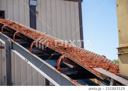 Conveyor belt transporting mulch at a landscaping supply facility on a sunny day Conveyor belt transporting mulch at a landscaping supply facility on a sunny day 132883529
