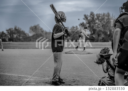 Young player waits at bat as pitcher throws baseball during a game in a local park on a cloudy afternoon 132883530
