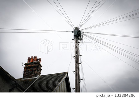 Wooden utility pole with multiple overhead wires near house chimney under cloudy sky Wooden utility pole with multiple overhead wires near house chimney under cloudy sky 132884286