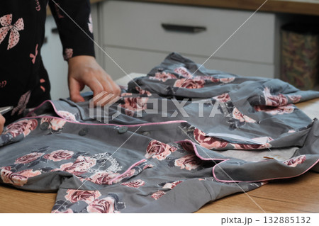 A woman is reviewing pajamas. She is examining the shirt. The pajamas consist of pants and a button-up shirt. A woman is reviewing pajamas. She is examining the shirt. The pajamas consist of pants and a button-up shirt. 132885132