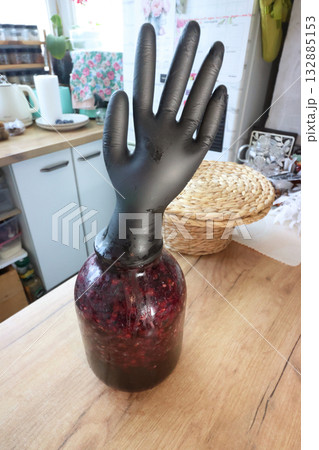 A glass jar with fermenting grapes. A black rubber glove is put on the jar. The glove is inflated by fermentation gases. Making homemade grape wine. Oblique Angle. A glass jar with fermenting grapes. A black rubber glove is put on the jar. The glove is inflated by fermentation gases. Making homemade grape wine. Oblique Angle. 132885153
