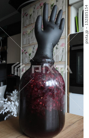 A glass jar with fermenting grapes. A black rubber glove is put on the jar. The glove is inflated by fermentation gases. Making homemade grape wine. 132885154