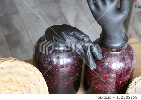 Two glass jars with fermenting grapes. Black rubber gloves are put on the jars. Making homemade grape wine. Oblique Angle. Two glass jars with fermenting grapes. Black rubber gloves are put on the jars. Making homemade grape wine. Oblique Angle. 132885159