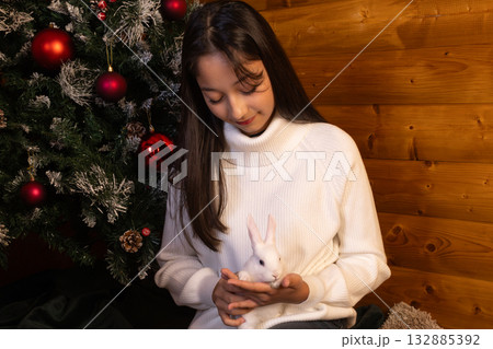 woman is gently holding a small white rabbit near Christma tree 132885392