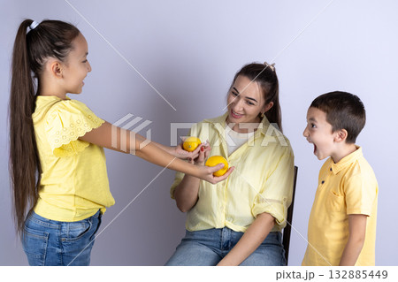 girl is offering a lemon to the woman, while the boy looks on with an open mouth girl is offering a lemon to the woman, while the boy looks on with an open mouth 132885449