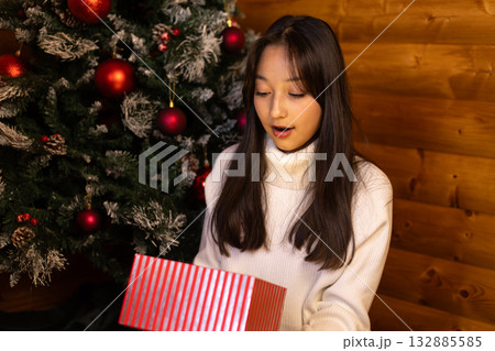 A woman with a surprised expression is opening a Christmas gift 132885585