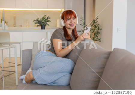 Young woman with wireless headphones listens to music from smartphone relax calm rest gentle smile Young woman with wireless headphones listens to music from smartphone relax calm rest gentle smile 132887190