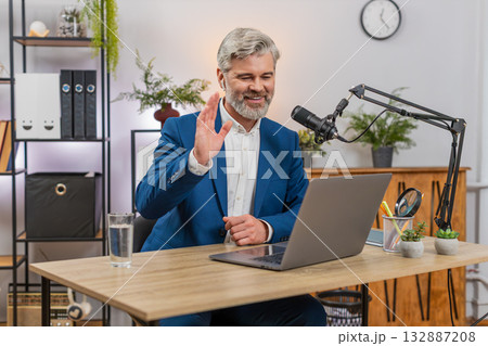 Middle-aged businessman records podcast on studio microphone gesturing actively sharing live ideas Middle-aged businessman records podcast on studio microphone gesturing actively sharing live ideas 132887208