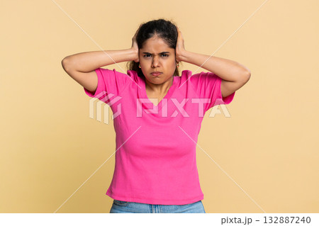 Indian woman abruptly covers ears with hands, expressing discomfort from loud annoying sound noise Indian woman abruptly covers ears with hands, expressing discomfort from loud annoying sound noise 132887240