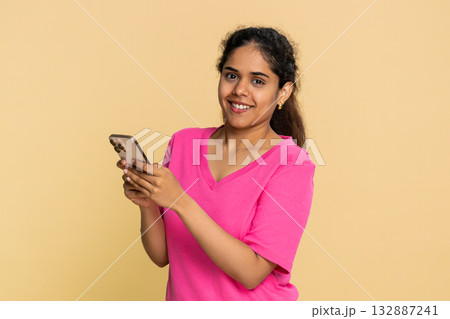 Indian woman smiling holding smartphone, actively texting message, cheerfully engaging online chat Indian woman smiling holding smartphone, actively texting message, cheerfully engaging online chat 132887241