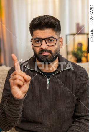 Indian young man showing serious NO gesture on sofa at home, expressing disagreement with frown Indian young man showing serious NO gesture on sofa at home, expressing disagreement with frown 132887294